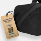 A black bag with a tag promoting recycled ocean plastic fabric and a QR code for more info.
