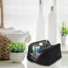 Black toiletry bag with toiletries on a countertop beside a plant and a basket with towels.