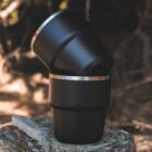 Two black metal cups stacked outdoors on a wooden surface, with a blurred natural background.