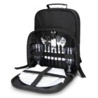Black picnic backpack open to show cutlery, plates, glasses, and napkins neatly packed inside.