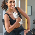 Smiling woman in workout clothes holding a water bottle at the gym.