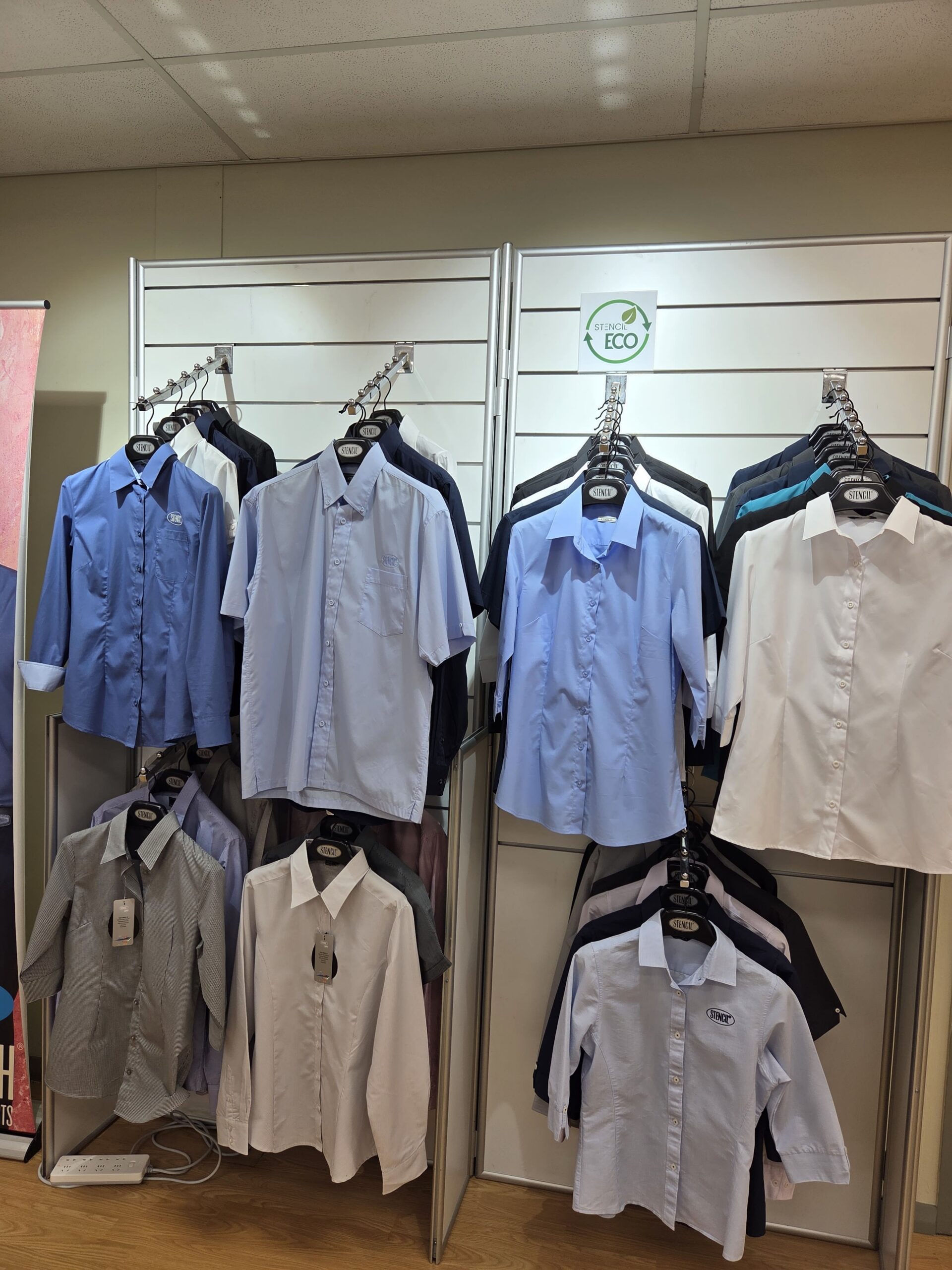 Assorted collared uniforms on hangers, displayed on a store rack with an ECO sign above.