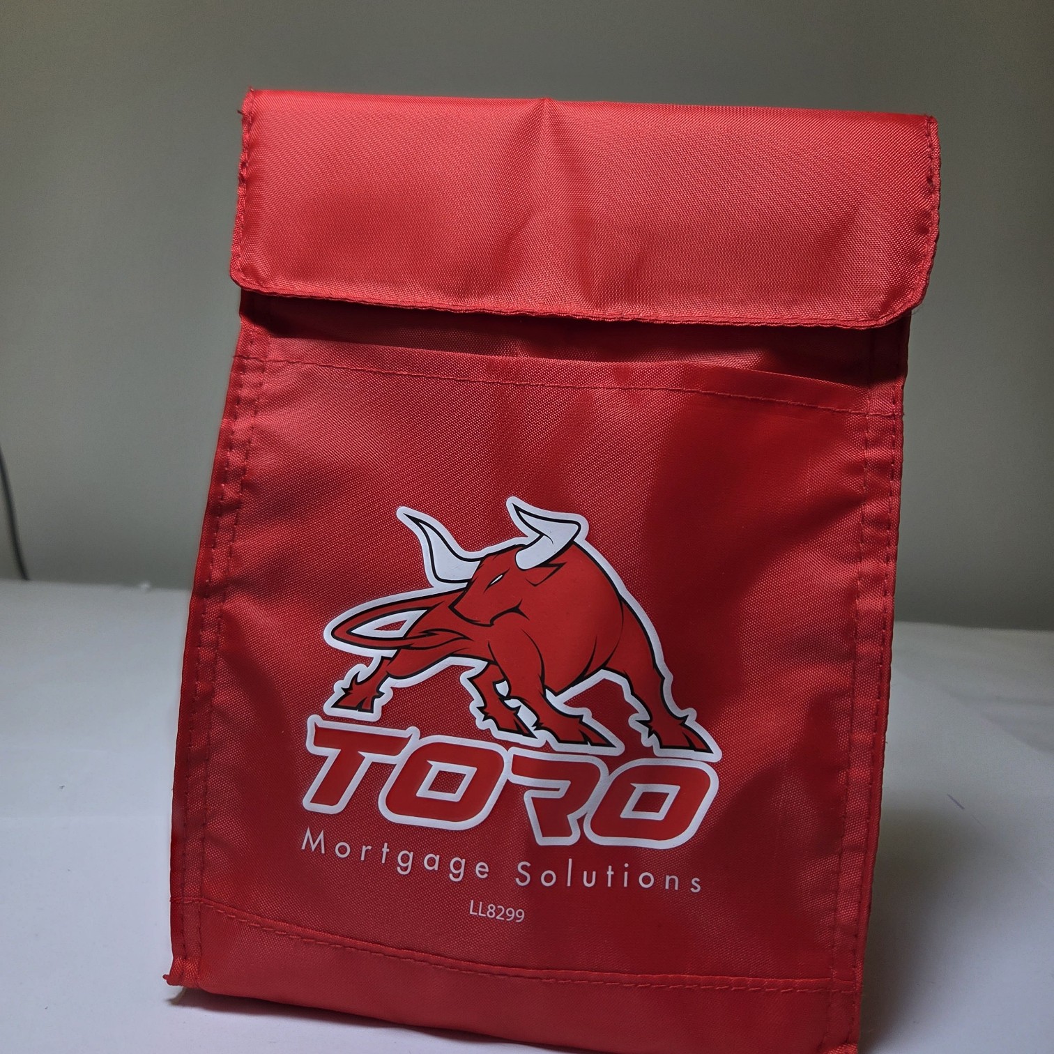 Red insulated lunch bag in TORO branding colours, featuring a charging bull logo and company name.