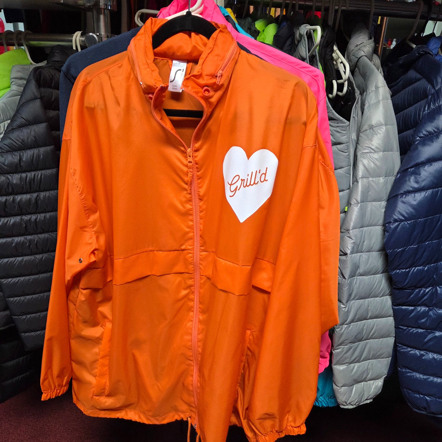 Orange jacket with Grilld in a white heart, a nod to product trends Sydney 2026.