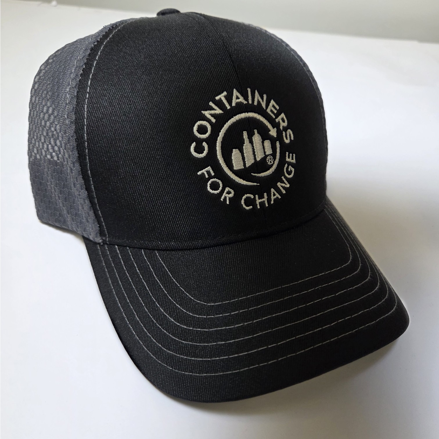 Black Containers for Change cap featuring branding colours and white logo on a white surface.