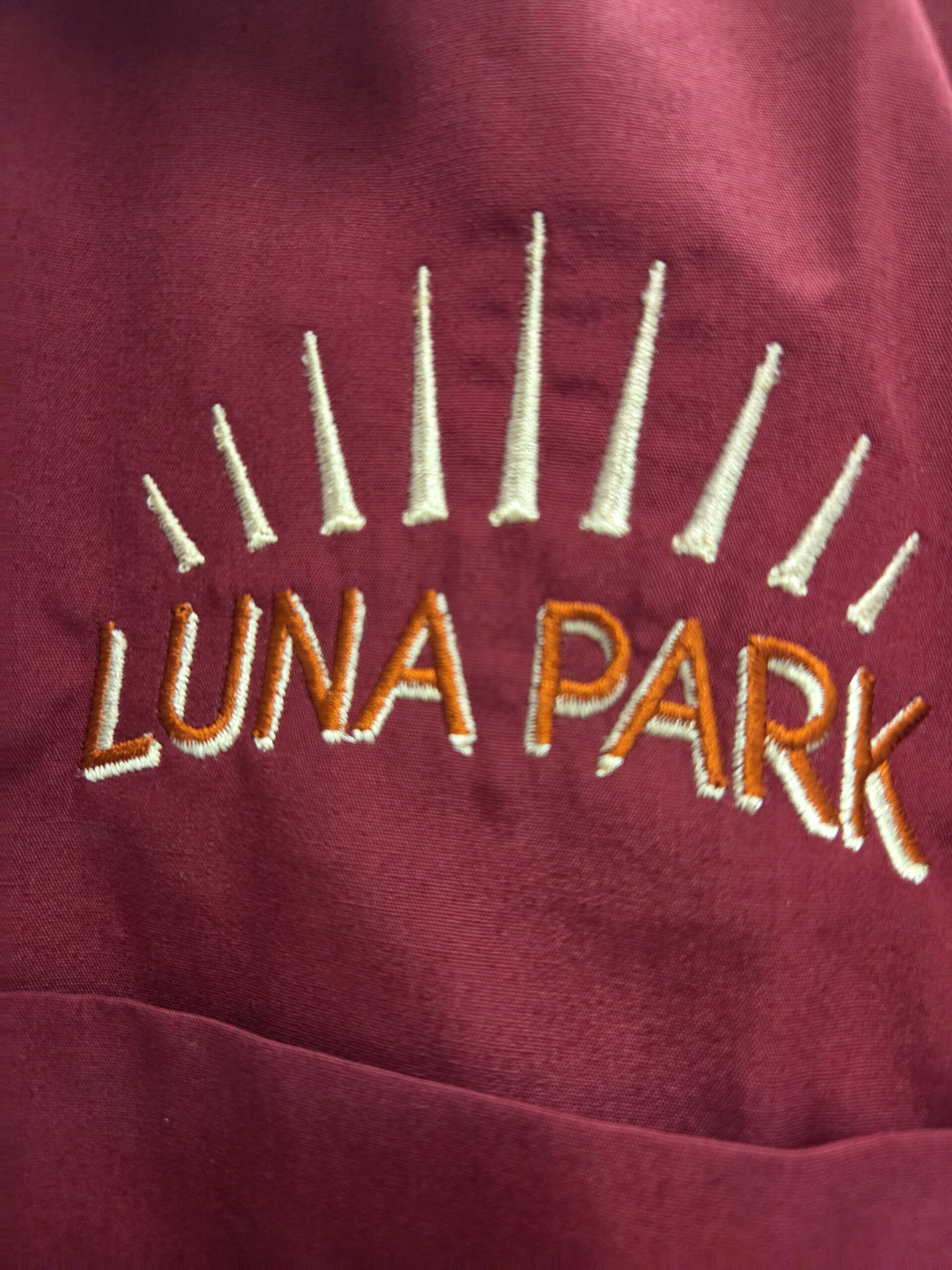 Maroon fabric features LUNA PARK and rays in yellow-orange embroidery vs screen printing.