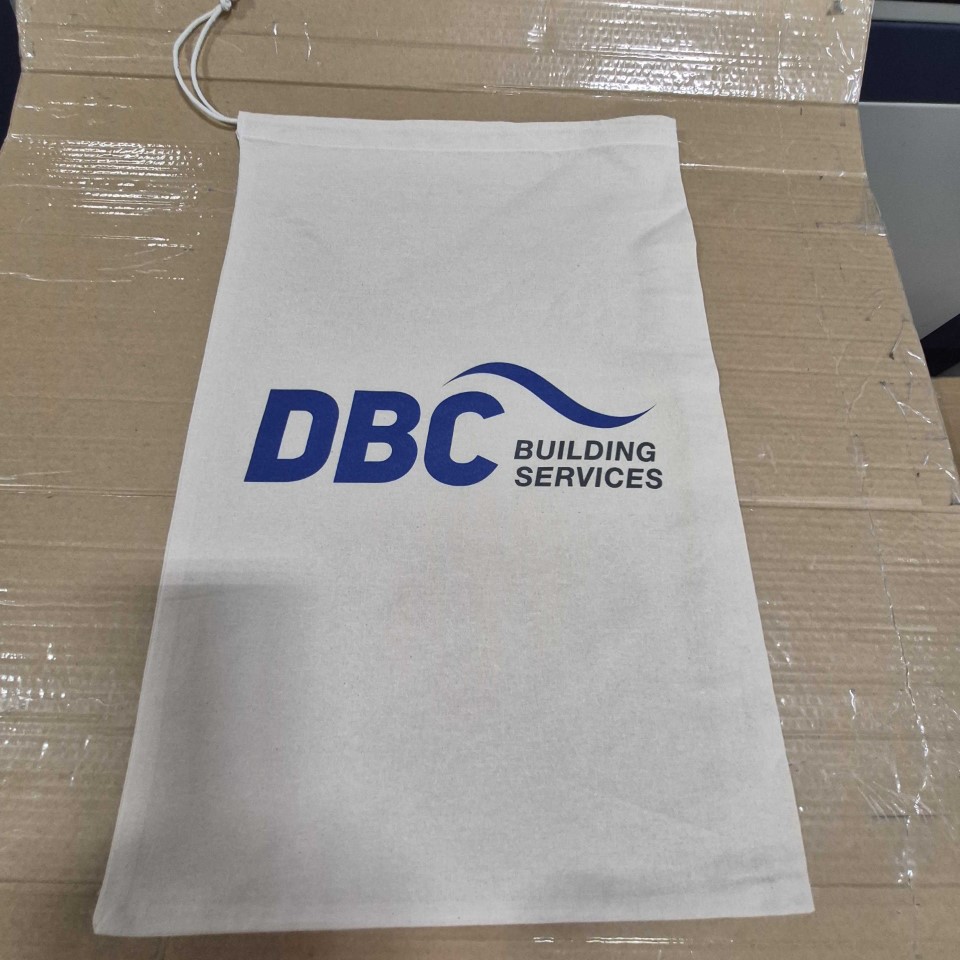 White drawstring bag with DBC Building Services logo in blue, lying on a cardboard surface.