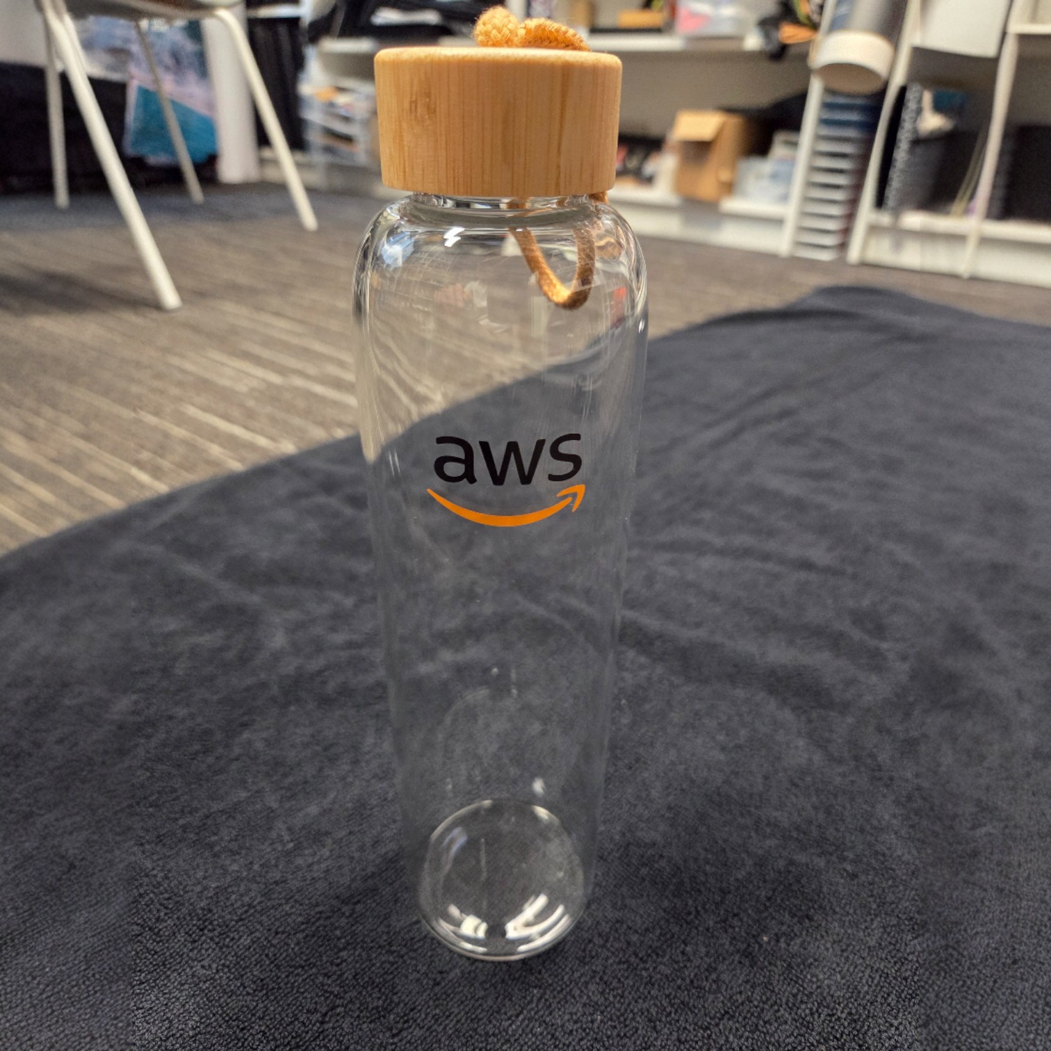 Clear glass bottle with bamboo lid and AWS logo, reflecting merchandise trends 2026.