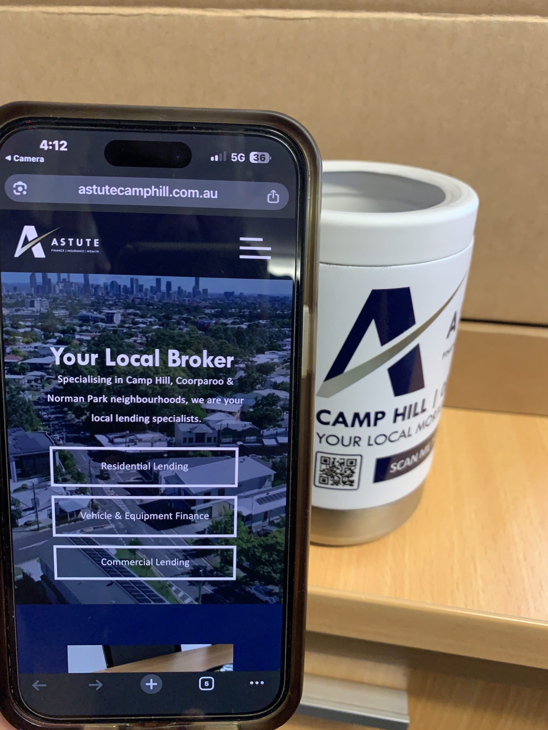 A phone displays Astute Financial’s site beside a branded container on a wooden desk.