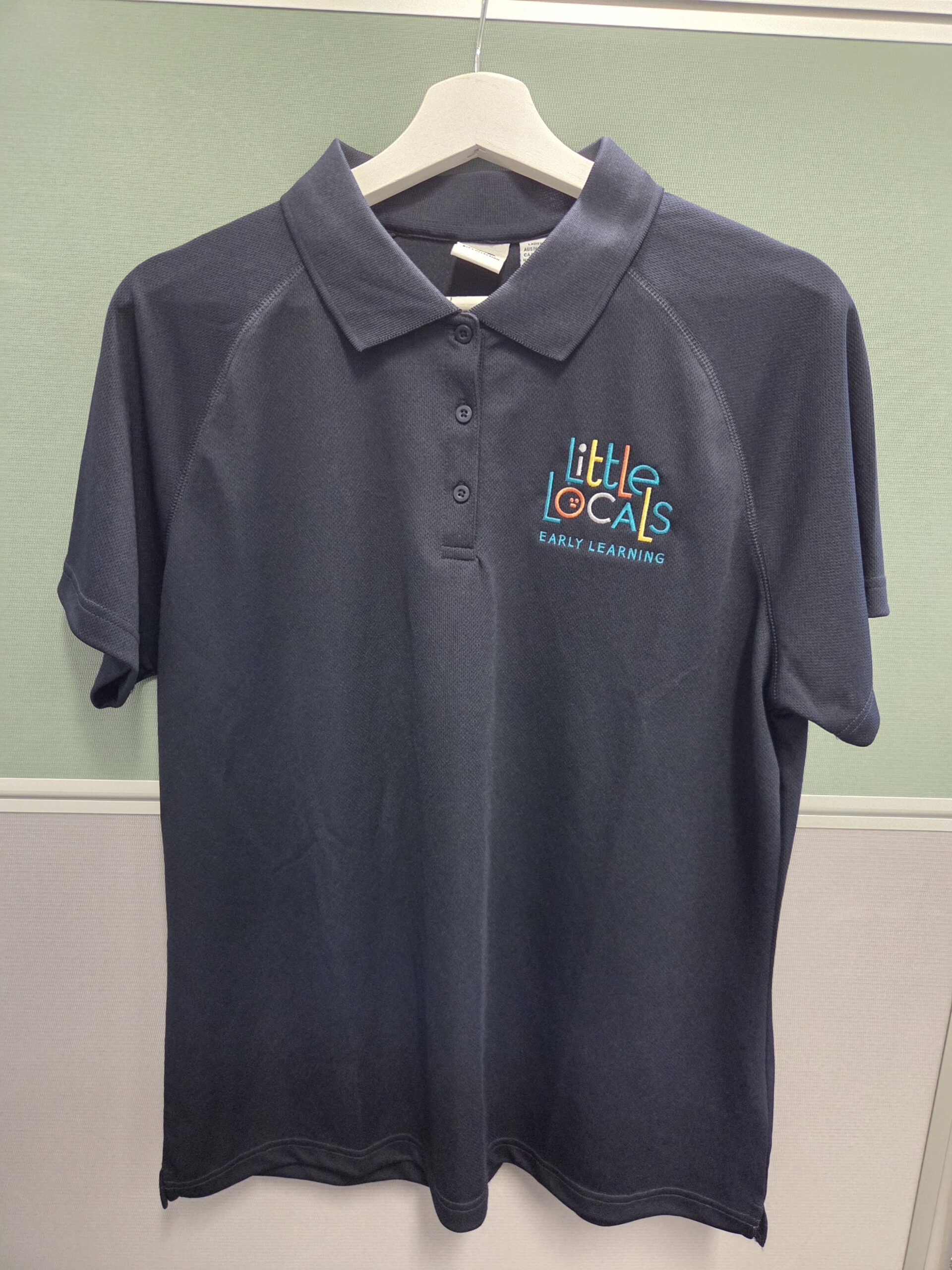 Dark polo shirt on hanger with embroidered Little Locals logo—see embroidery vs screen printing.