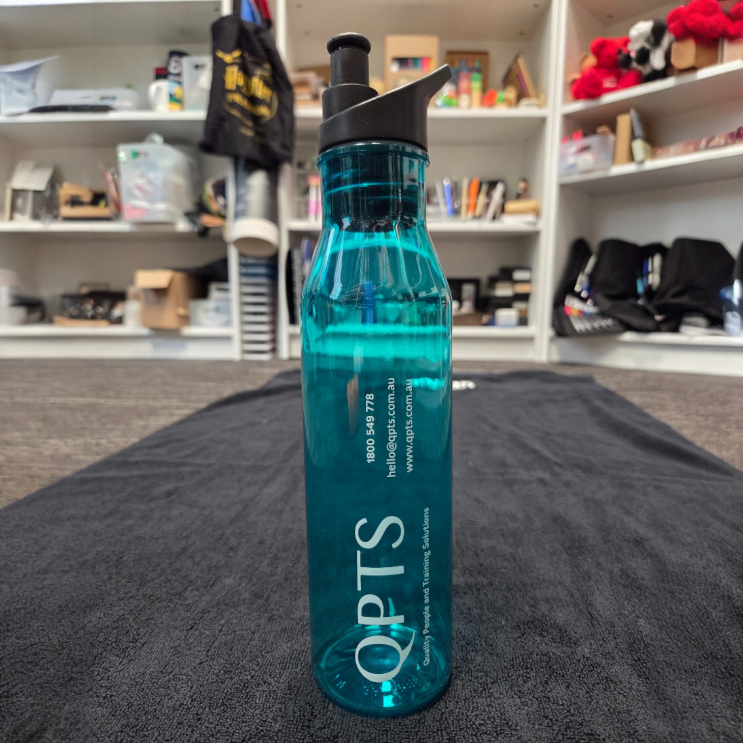 A blue OPTS water bottle on a black mat highlights bamboo vs plastic promotional items.