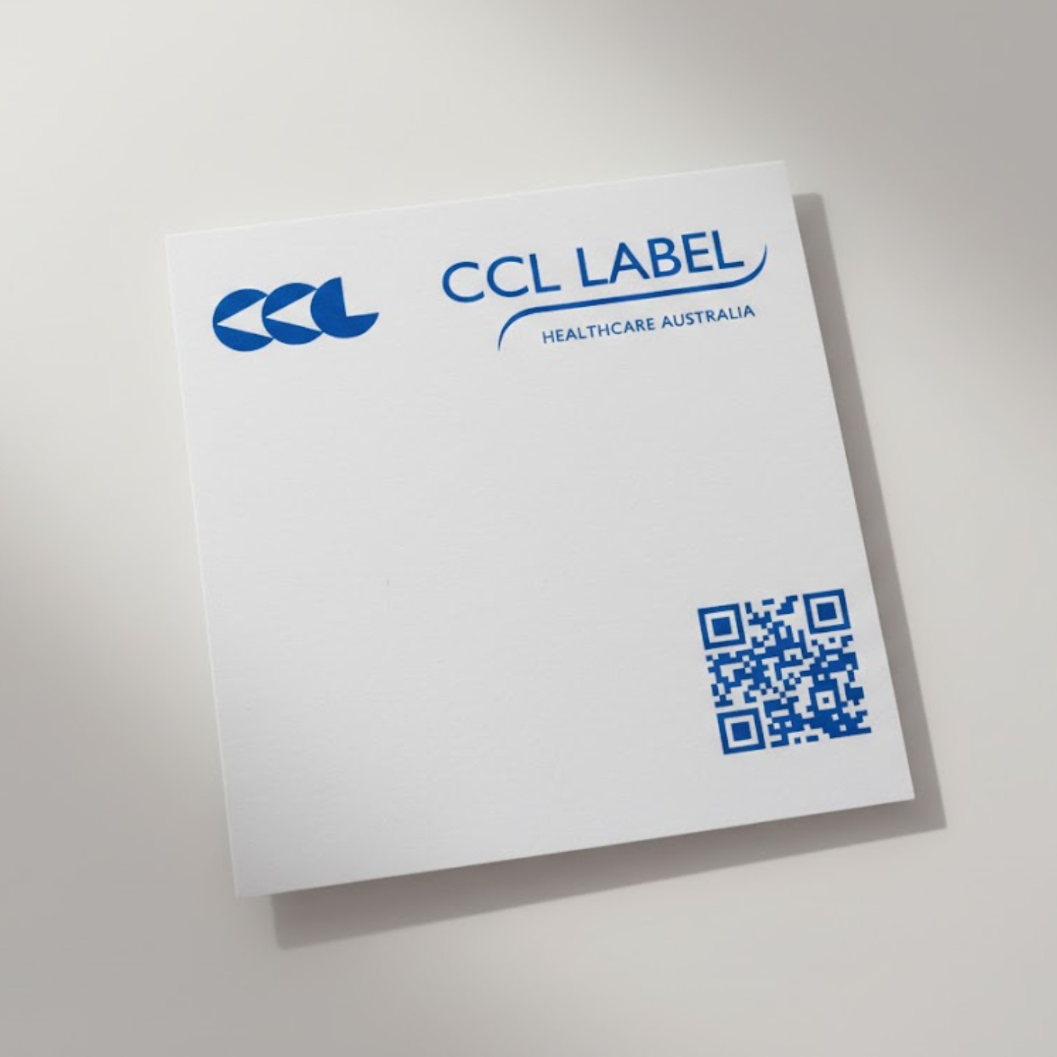 White card with CCL LABEL HEALTHCARE AUSTRALIA, blue QR code, and a sticky notes promotional item.