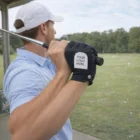 Man in a cap at the driving range wears Customized Golf Gloves while holding a golf club.