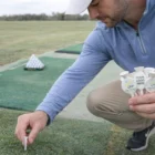 Man placing Tees on grass, holding golf tees with blank logo space.