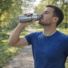 Man in blue shirt sips from an X-Stream BPA Free Drink Bottle on a sunny park path.