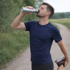 Man in navy t-shirt uses Action Water Bottles while stretching on a gravel path outdoors.