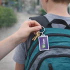 Hand attaches keys with a purple Keystash Key Rings Rectangle to a teal backpack.