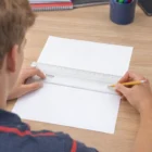 Person using a Kumbus Magnifying Rulers and pencil to draw a line on blank paper.