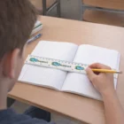 A student uses a Flipper Rulers and pencil to draw a line in a graph paper notebook.