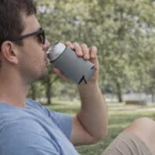 Man relaxes on sunny grass, sipping a drink with Collapsible Coolers With Base Stocked.