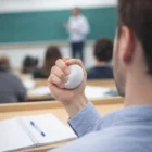 A student squeezes a Cushy Stress Ball in class while taking notes as the teacher writes.
