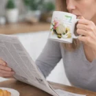 Woman enjoying coffee from a Tuscan Coffee Mug while reading the newspaper at a table.
