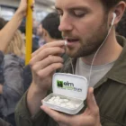 A man takes a mint on a crowded train, holding a Hetzel Mint Tins elm wildlifetours tin.