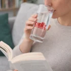 Woman reading a book while sipping water from Medium Cambridge Glass Tumblers.