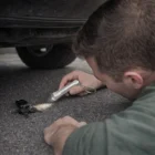 Man uses Budget Titan Torches to search for car keys under a vehicle on the ground.