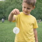 Smiling boy in yellow shirt playing with Promotional Cheap Yoyo Toys in a park.