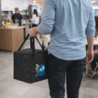 Person carrying The Arctic Coolers bag with a colorful logo in an office kitchen area.