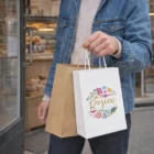 Person holding Vex Paper Carry Bags Small with logo, standing outside a bakery.