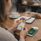 Woman with Razzle Silicone Phone Wallet, coffee, pastry, and cards at a café table.
