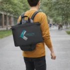 Man outdoors with a black Rokka Satchel Bag over his backpack, wearing a mustard sweater.