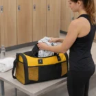 Woman packing clothes into a yellow and black Noxa Duffle Bag in a locker room.
