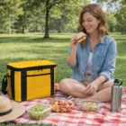 Woman picnicking on red checkered blanket with food, Yowie Cooler Bags, and a water bottle.