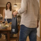 Man holding a Vevino Wine Carrier walks toward a woman at a dinner table with food and drinks.