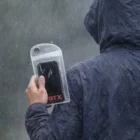 Person in a raincoat uses Wixel Phone Pouches to protect their phone during heavy rain.