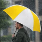 Man walks in rain holding Becker Logo Printed Sports Umbrella.