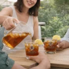 Woman pours iced tea into Zaxen Glass Tumblers labeled Legacy Hotels & Resorts outdoors.