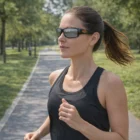 Woman wearing Hunter Sunglasses jogging on a park path amid green trees.