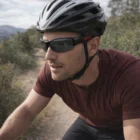Man cycling outdoors in Genie Printed Sports Sunglasses and helmet on a dirt path through greenery.