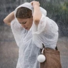 Woman in a Branded Emergency Rain Coat In Balls stands in heavy rain, hood over her head.