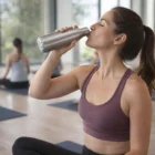 Woman in workout clothes drinks from a Trance Branded Aluminium Bottle in a yoga studio.