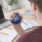 Person squeezing a Globe Stress Toy at a desk with notebooks and a laptop.