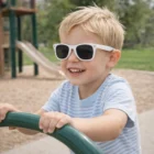 Smiling boy wears Soho Kids Sunglasses while playing outside at a playground.