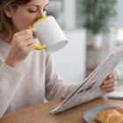 Woman enjoys coffee from a Mugs With Inner Colour Print while reading and eating a croissant.