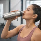Woman in workout clothes drinks from a Savanna Metal Water Bottle at the gym.