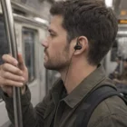 Man with Astrid Bluetooth Earbuds, wearing green jacket and black backpack on subway.