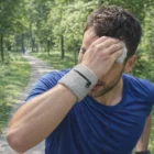Man in blue shirt wipes sweat with Toffa Pocket Wrist Sweat Bands while jogging on a forest path.
